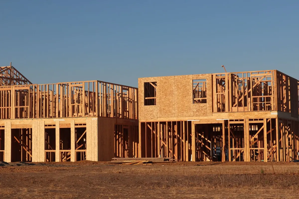 Timber frames of new two-storey houses on a cleared lot under a clear sky