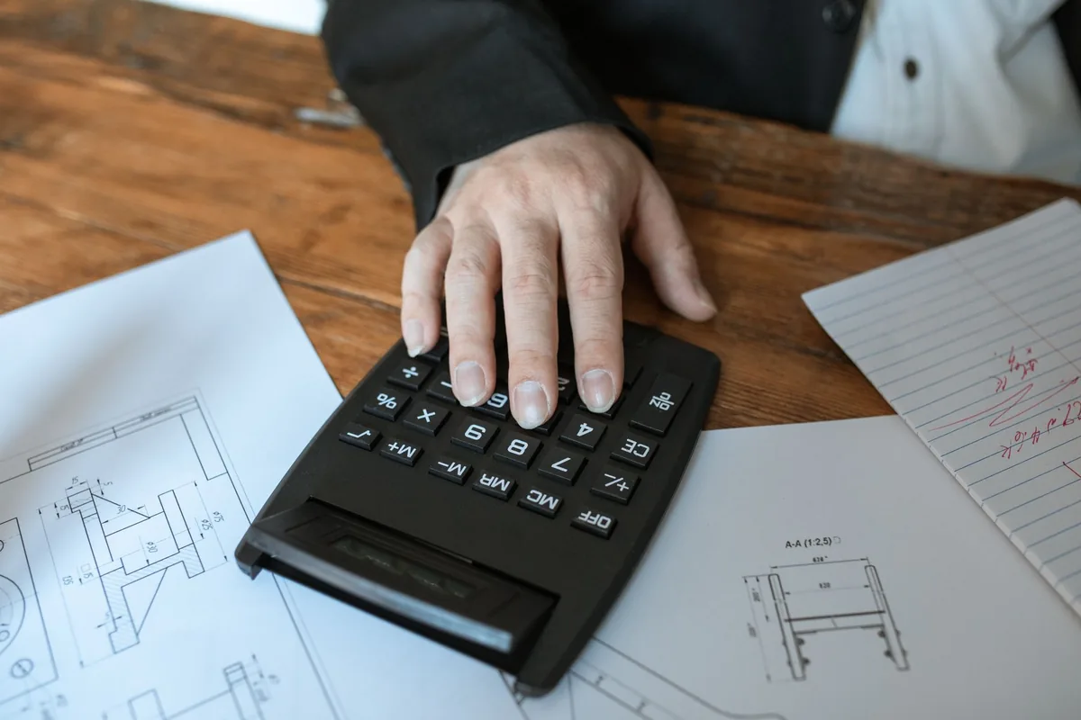 A hand using a calculator on top of architectural drawings