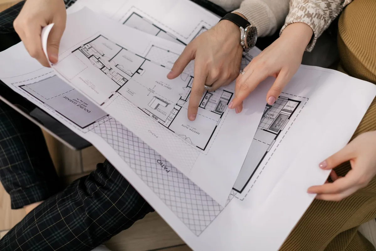 Two people pointing at a house floor plan
