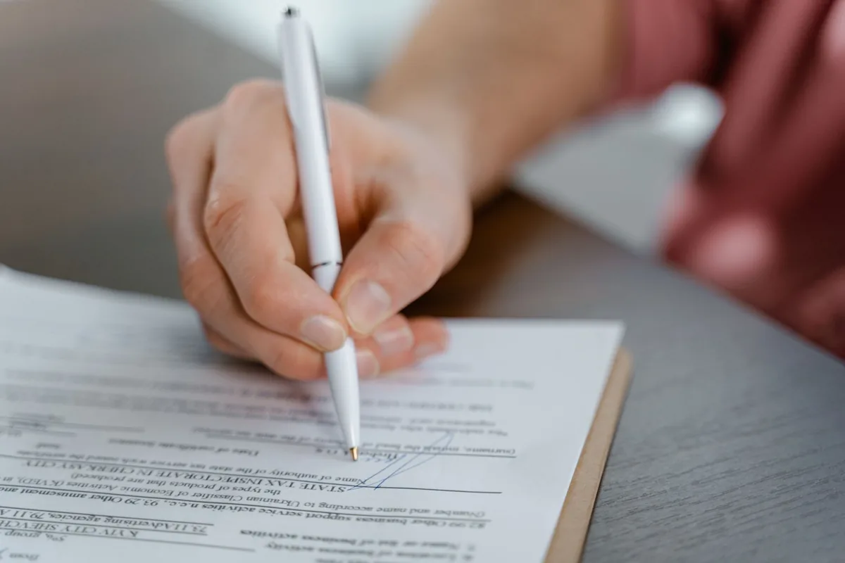 A hand signing a printed document with a white pen