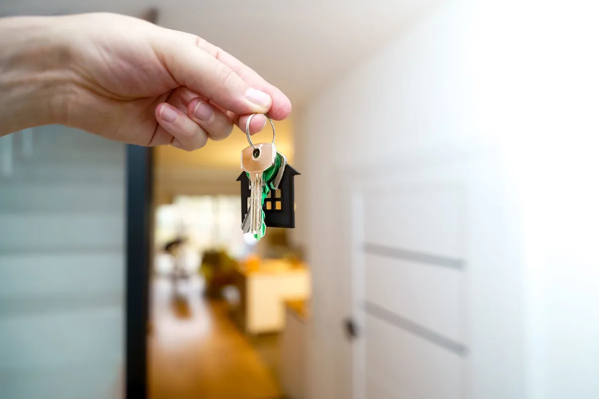 A hand holding house keys on a house-shaped key ring