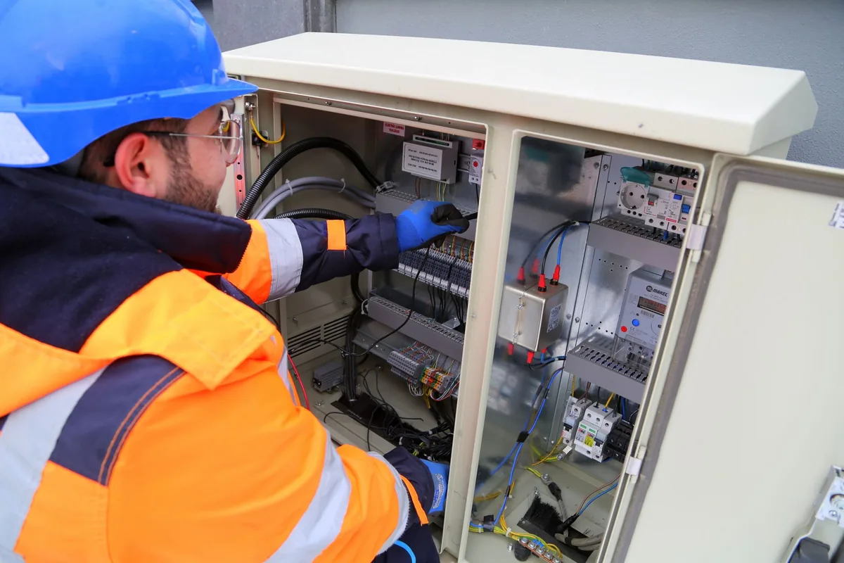 An electrician in a hard hat and high-visibility jacket working inside an electrical cabinet