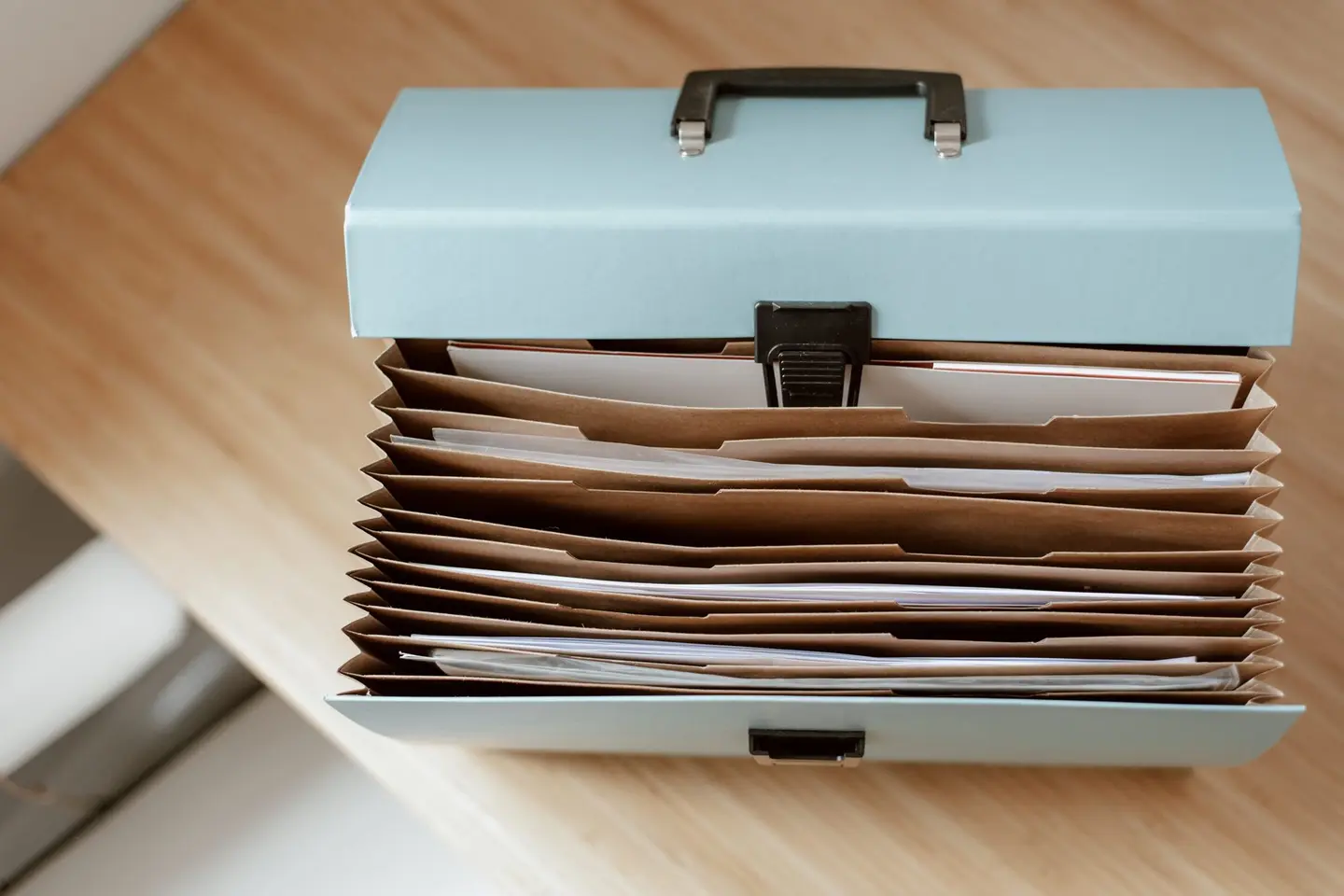 An open expanding file box full of paper documents on a desk