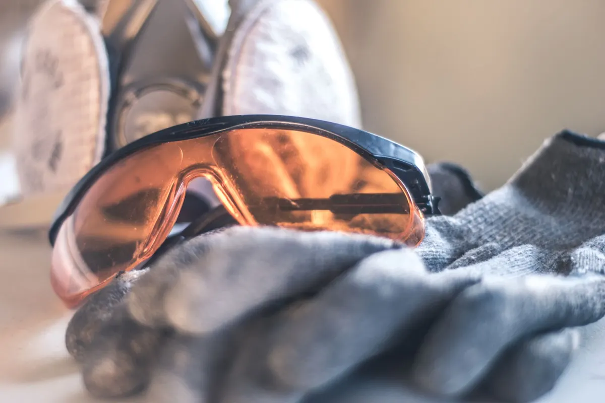 A half-face respirator, safety glasses and work gloves on a bench