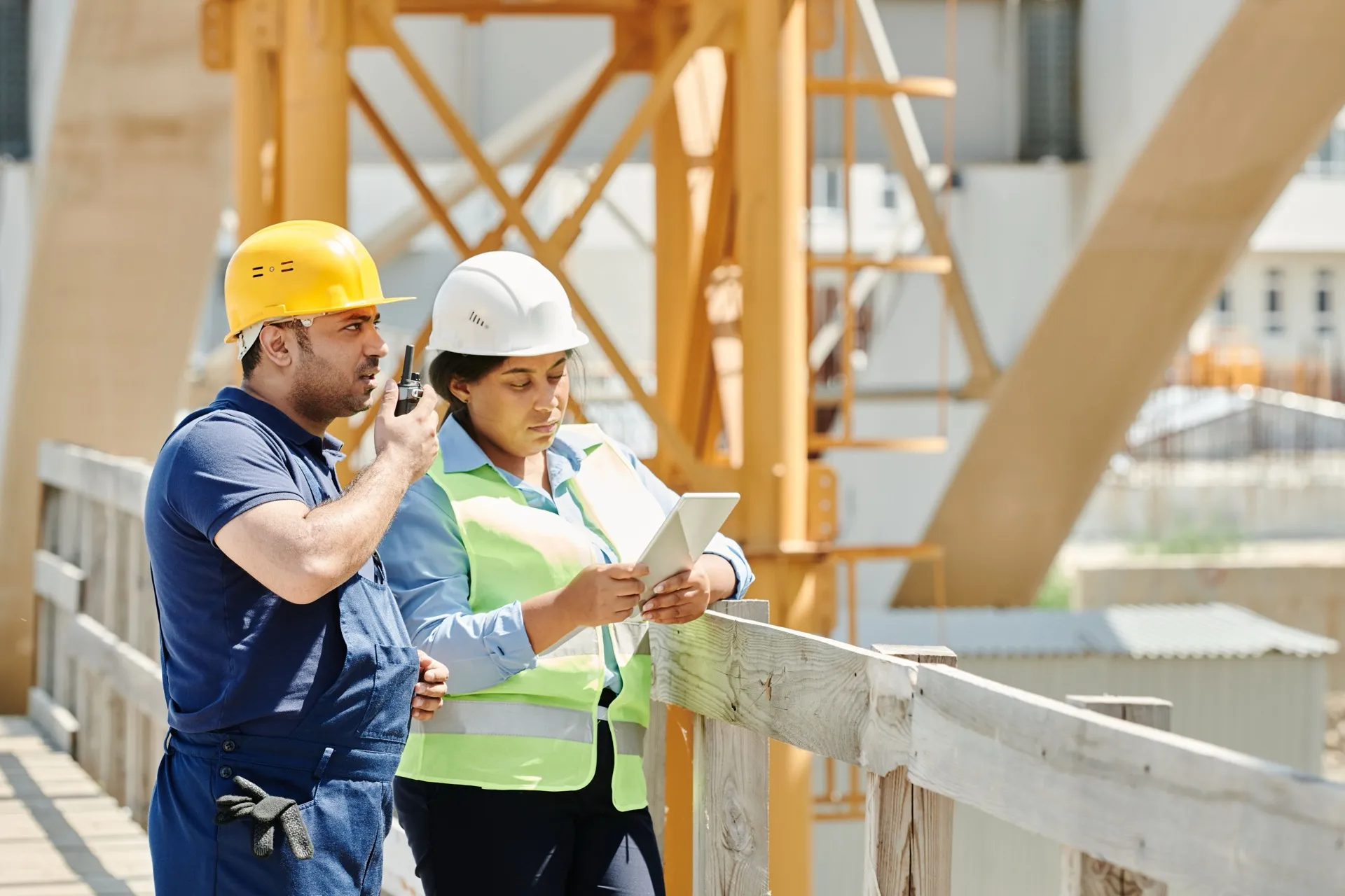 Two construction professionals in hard hats comparing figures on a tablet at a building site