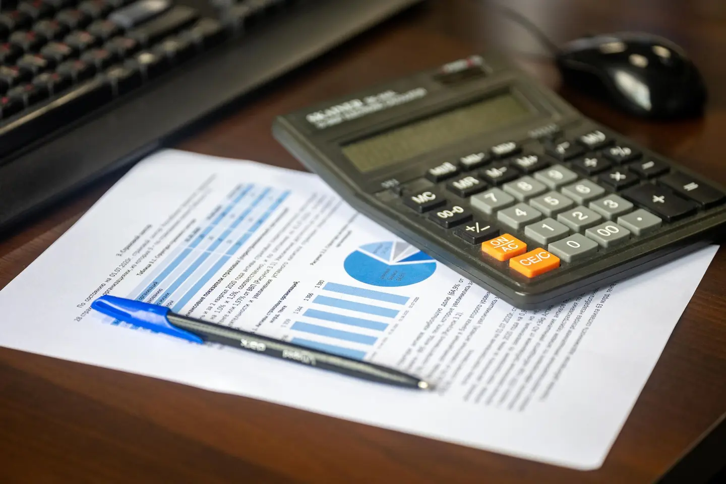A calculator resting on printed financial charts beside a pen and a keyboard