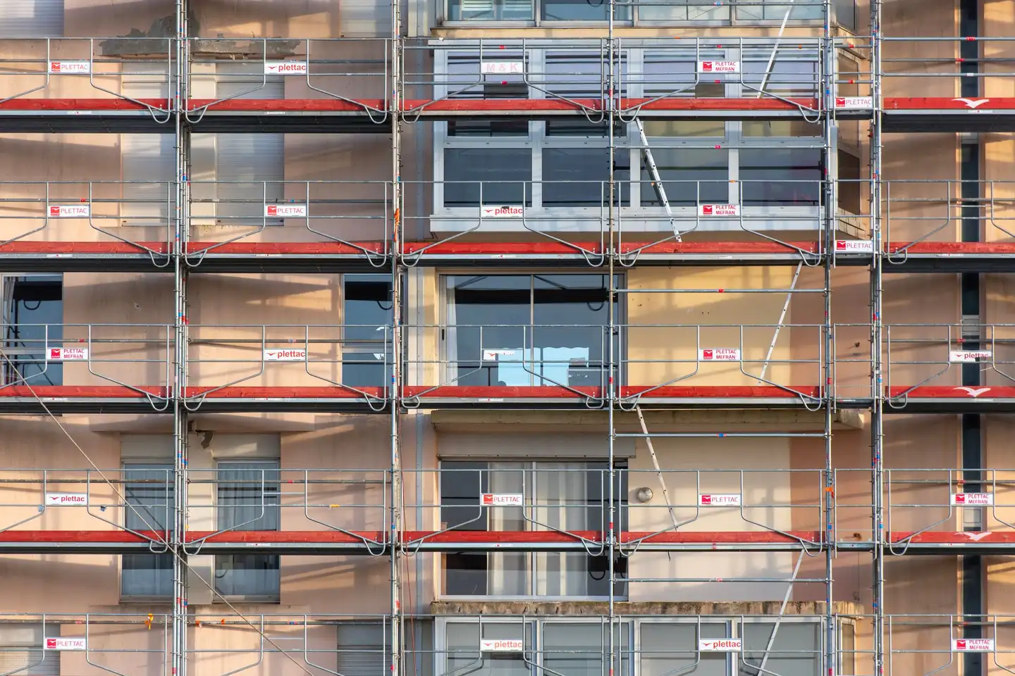 Scaffolding with red guard rails across the facade of an apartment building