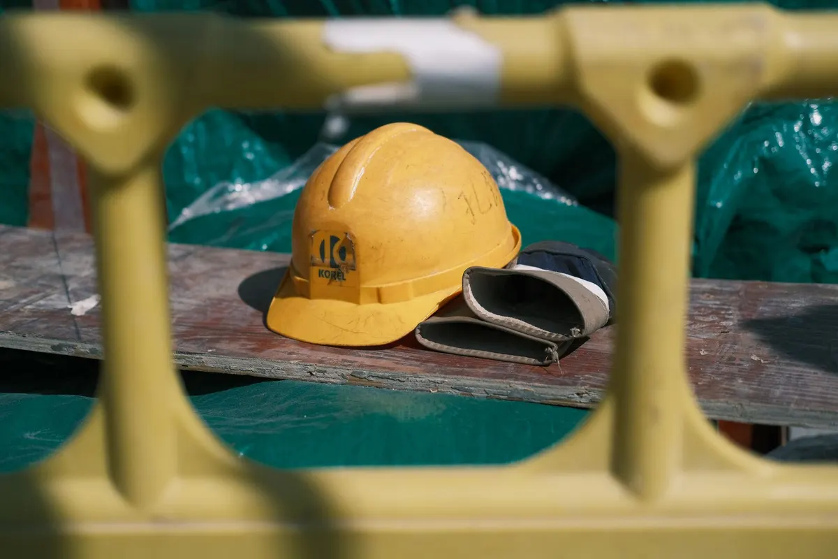 A yellow hard hat and gloves seen through a plastic safety barrier