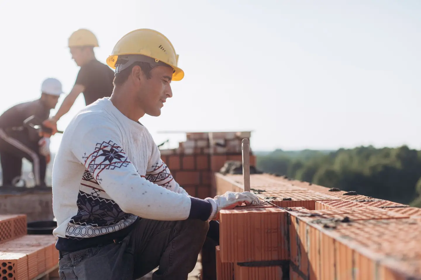 Bricklayers in hard hats laying clay blocks on a building site