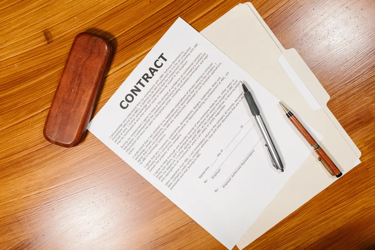 A printed contract with two pens and a wooden pen case on a timber desk