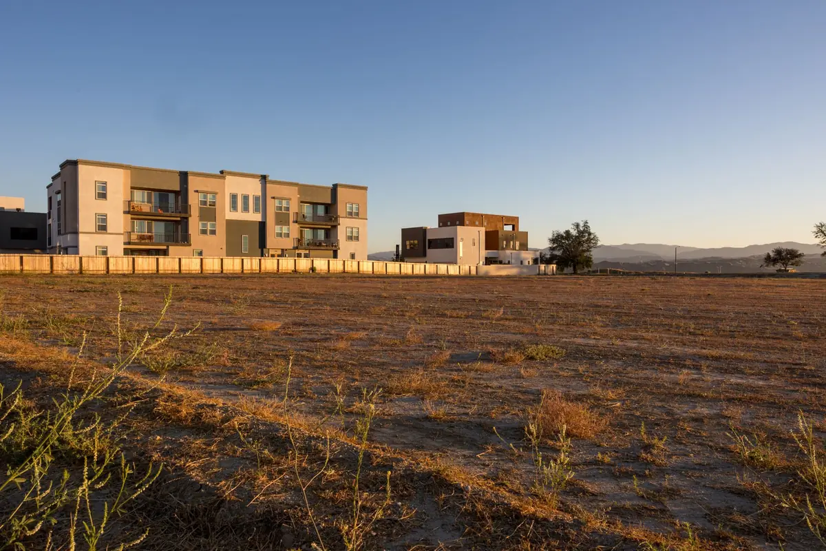 An open field beside new apartment blocks with hills in the distance