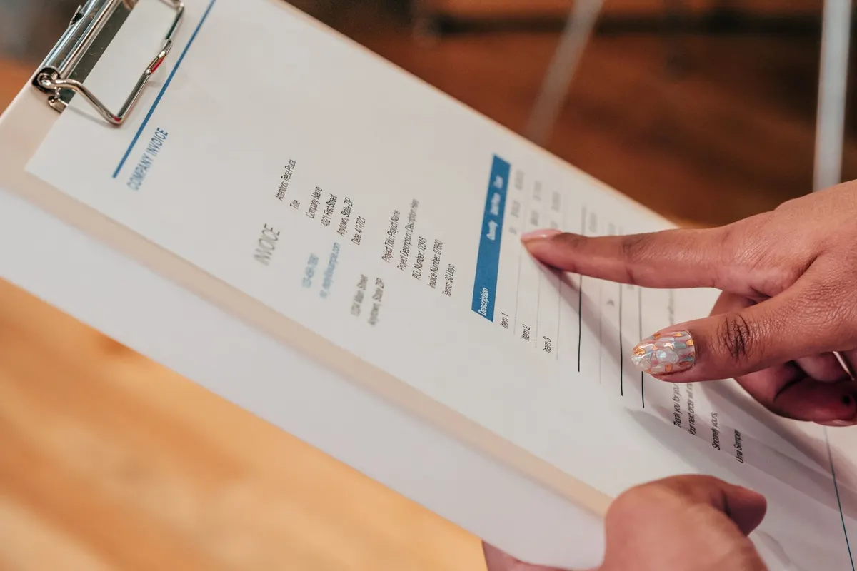 A hand pointing at line items on an invoice held on a clipboard