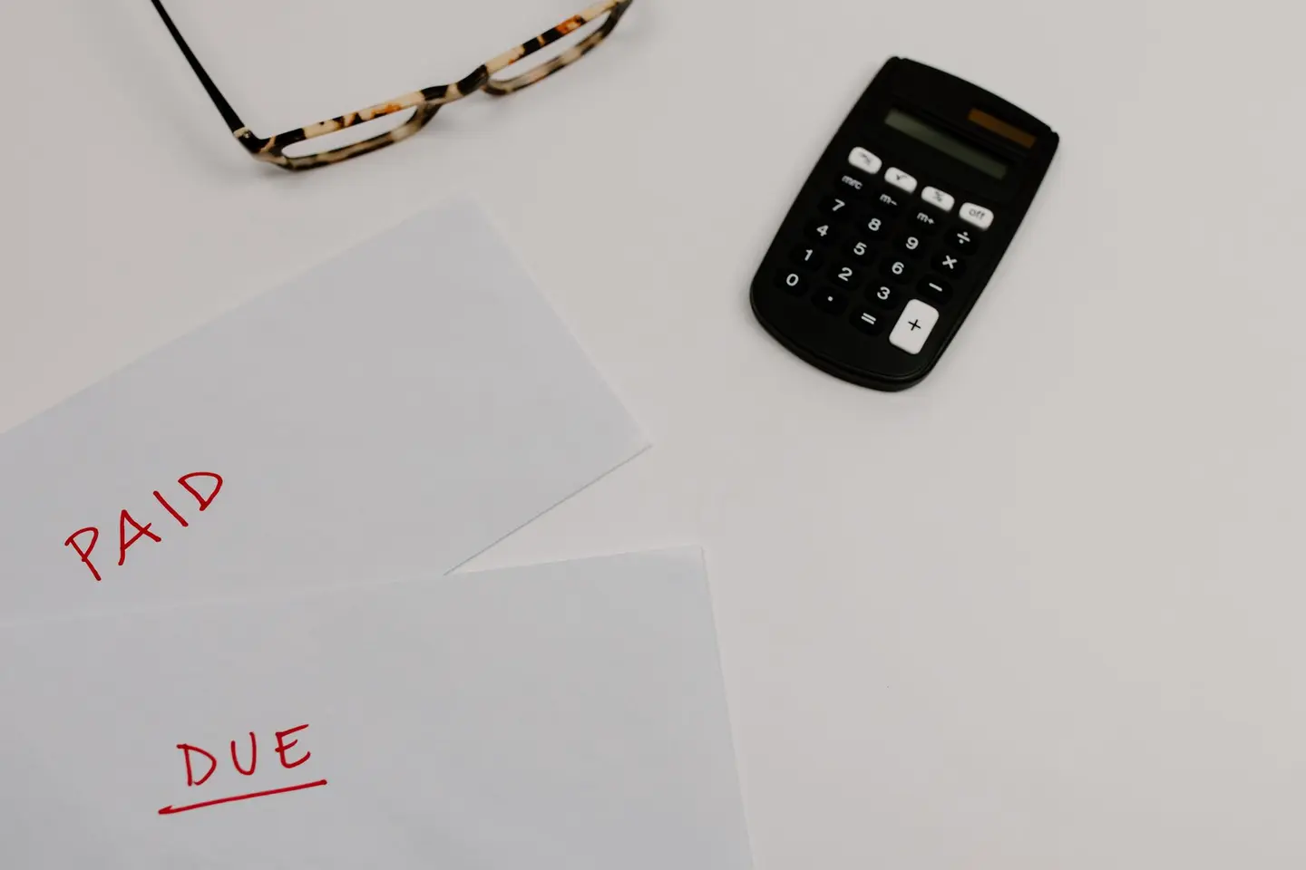 Two sheets of paper marked PAID and DUE beside a calculator and a pair of glasses