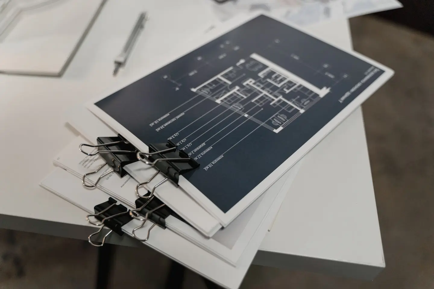 A pile of bound architectural drawings held together with black binder clips