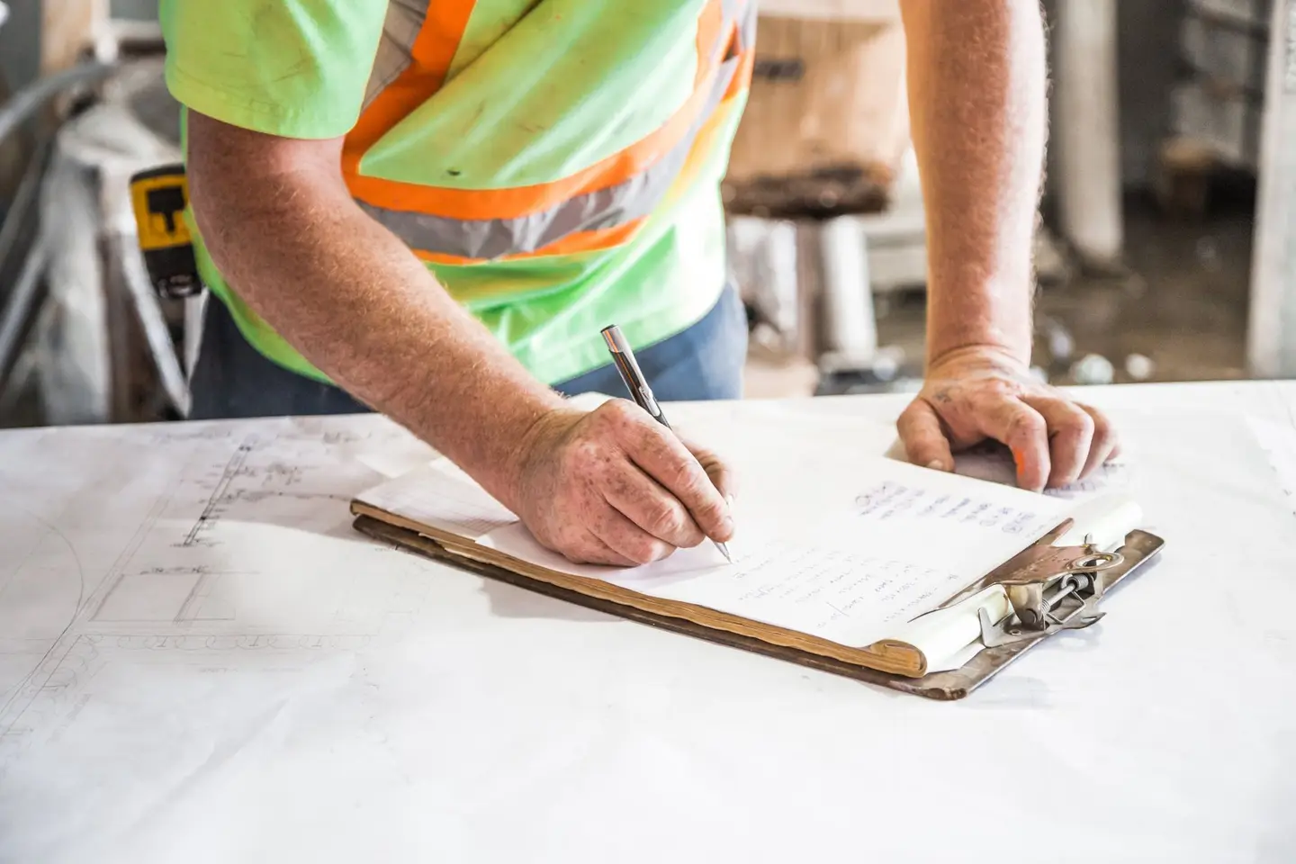 A worker in a high-visibility vest writing on a clipboard at a site table
