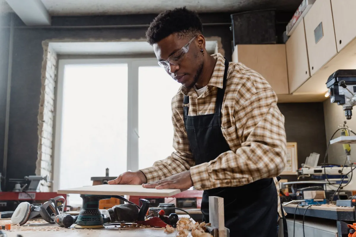 A trainee in safety glasses working at a bench in a woodwork shop