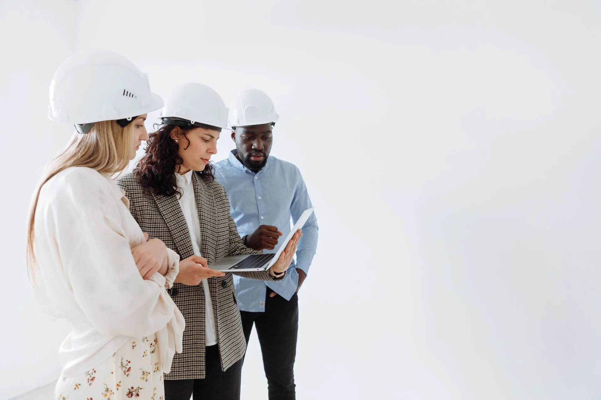 Engineers in hard hats reviewing plans on a laptop indoors
